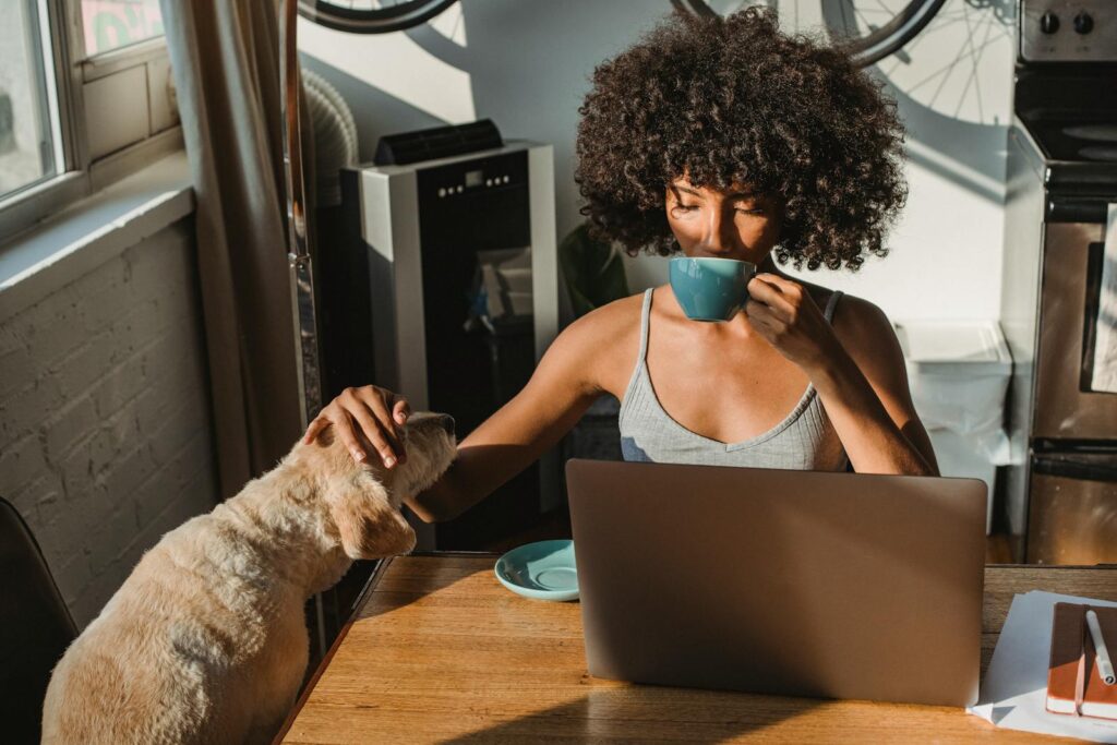 Get Started with Amazon FBA and Make Money Selling Products 1 Concentrated young black woman working remotely on netbook while sitting in room at table and drinking coffee while petting dog